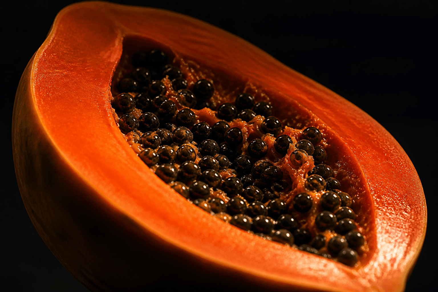 Cross-section of a ripe papaya, seeds glistening in the dark
