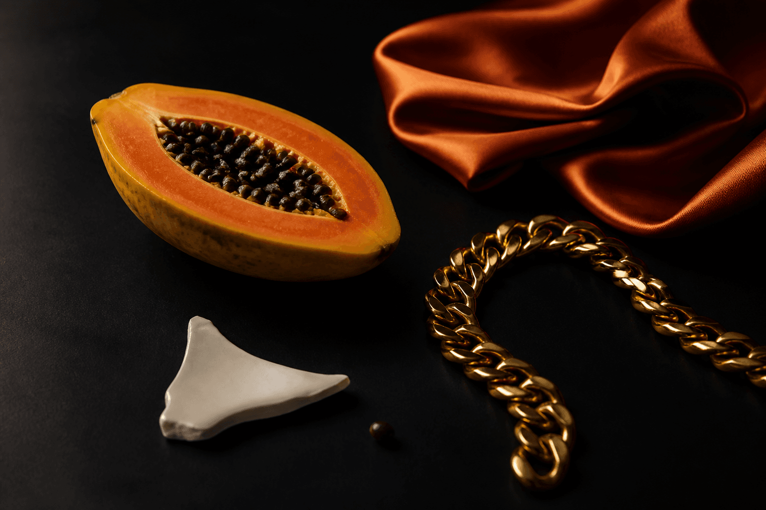 Still life of papaya, gold chain, and silk on black